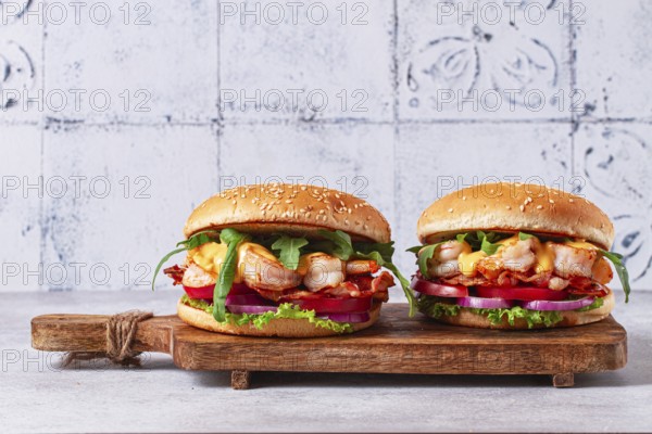 Two shrimp burgers and buns with sesame seeds, bacon, lettuce, tomatoes and onions, On a wooden board