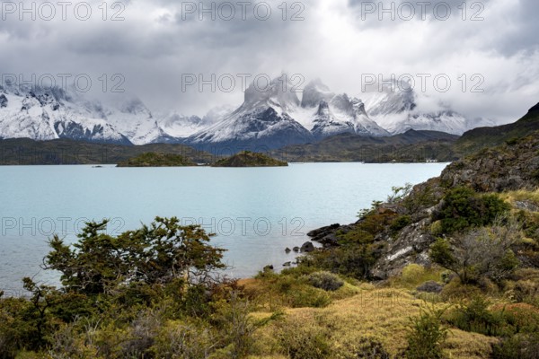 Cloudy mountain range Cuernos del Paine, shore of the blue lake Lago Pehoe in the evening light, dramatic sky, Torres del Paine National Park, Chile