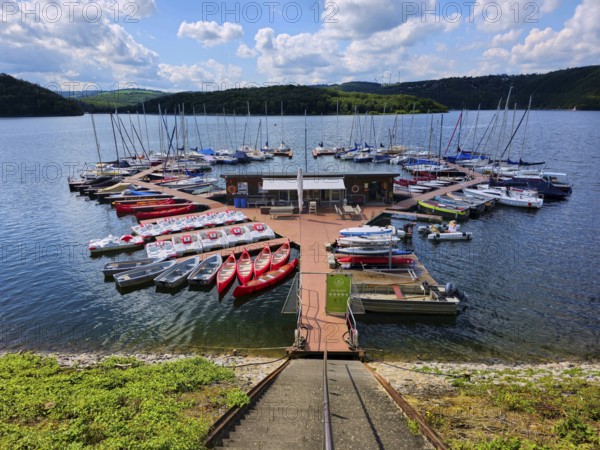 A colourful little marina with boats, sailing boats and pedal boats docked at a jetty on a lake, summer, Rursee, Rurtalsperre, Simmerath, Eifel National Park, North Rhine-Westphalia, Germany