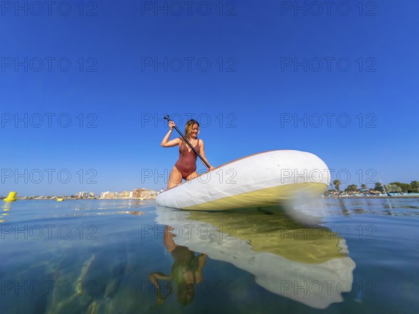 Young woman paddling on a stand up paddle board in the serene sea, soaking up the sun on a beautiful summer day along the coast