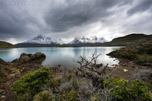 Cloudy mountain range Cuernos del Paine, shore of the blue lake Lago Pehoe in the evening light, dramatic sky, Torres del Paine National Park, Chile