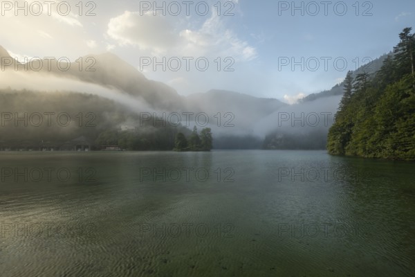 Mystical morning at Königssee in Schönau with boathouses and Christlieger. Sunrise and beautiful wafts of mist over the Königssee in the basin