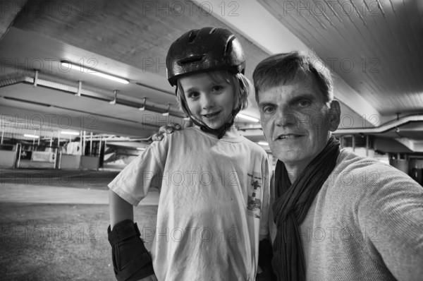 Boy, blonde, 6 years old, crash helmet, protective clothing, posing with older man for selfie, subway, urban, concrete, black and white, Stuttgart, Baden-Württemberg, Germany