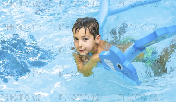 Happy boy enjoying playtime with an inflatable toy whale in a sparkling swimming pool, soaking up the sun during summer vacation