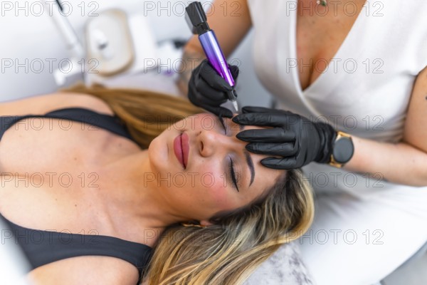 Beautician wearing black gloves using a dermopigmentation machine applying permanent eyeliner makeup on a client lying on a stretcher