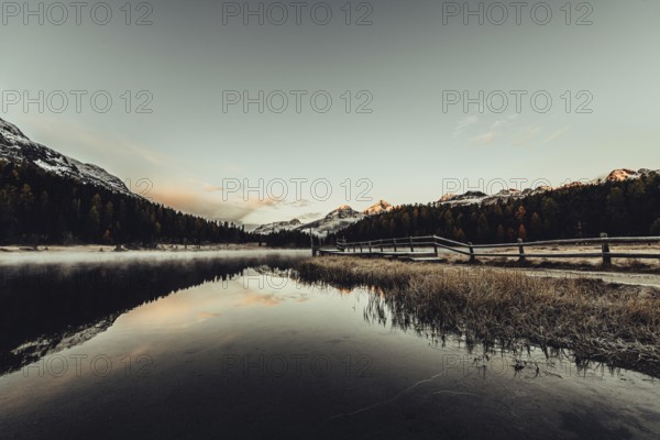 Lake Staz near Sankt Moritz in the Engadin in Switzerland. Morning atmosphere with fog in autumn. Water reflection and snow-covered mountains in the background