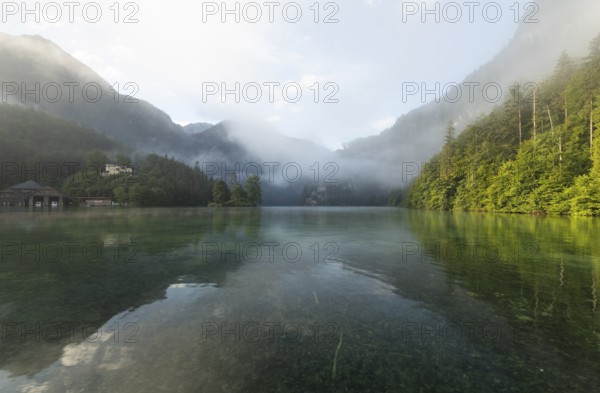Mystical morning at Königssee in Schönau with boathouses and Christlieger. Sunrise and beautiful wafts of mist over the Königssee in the basin