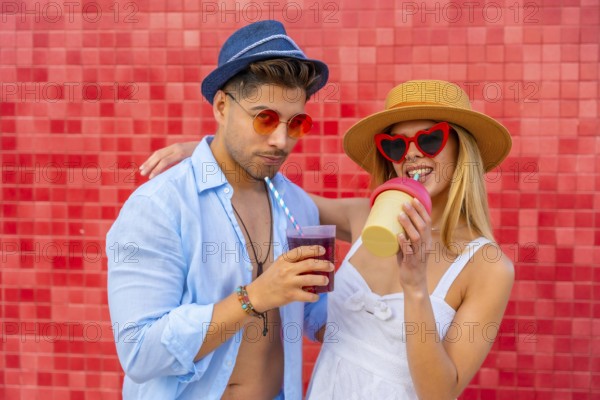 Happy couple enjoying colorful beverages on a summer day, showcasing trendy fashion and a vibrant backdrop