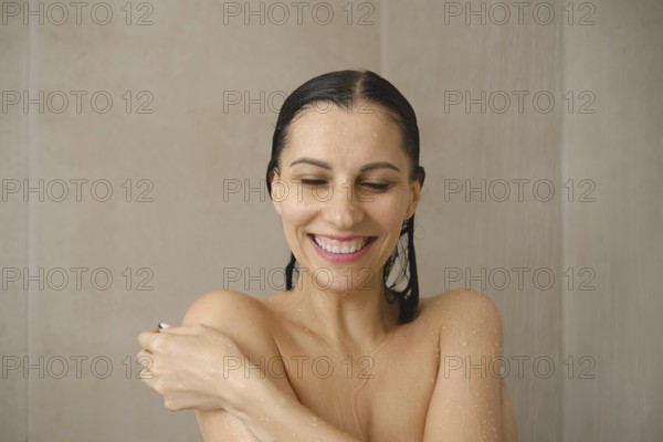 A woman stands under a gentle stream of water in a stylish bathroom, smiling and looking relaxed. Water droplets cascade down, highlighting a moment of self-care and tranquility during her shower