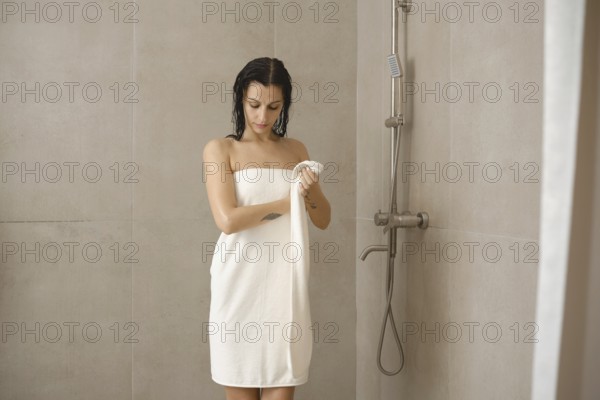 A young woman stands in a modern shower wrapped in a towel, drying her body. The neutral-toned tiles and minimalistic fixtures emphasize a serene atmosphere, creating a refreshing moment