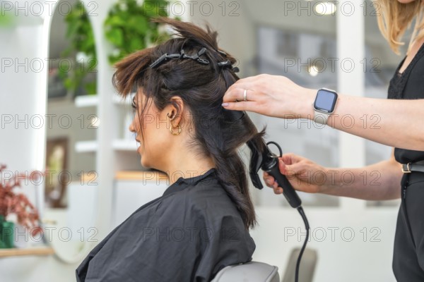 Hairdresser styling client's hair with curling iron in a modern beauty salon, creating a fashionable look