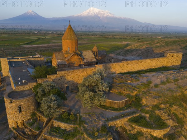 Historical monastery against a mountain backdrop in daylight surrounded by stone walls, aerial view, Chor Wirap monastery, deep dungeon, Ararat and Little Ararat in the background, located in Turkey, Ararat province, Armenia
