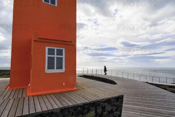 Orange lighthouse Skálasnagaviti or Svörtuloft with wooden plank path, walker, Skalasnagi, Öndverdarnes, Snæfellsnes peninsula, Snaefellsnes, Iceland