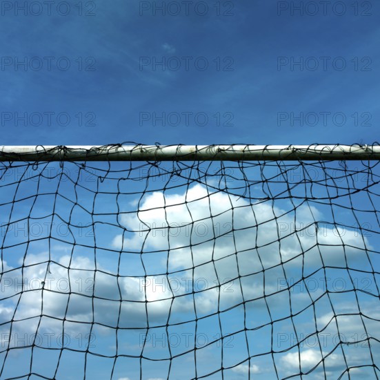 A football goal net stands prominently against a backdrop of a cloudy sky. The bright blue sky adds depth, showcasing the net's intricate design. It's a clear day perfect for outdoor sports