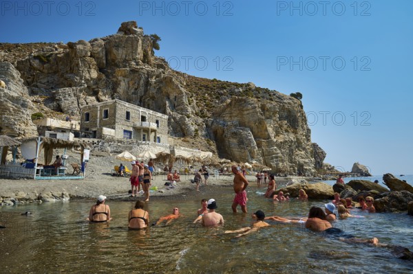 People enjoying the sun on the beach in front of a building and rocky coast, Embros Thermal Baths, Kos, Dodecanese, Greek Islands, Greece