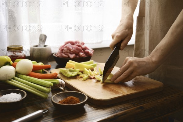 Hands skillfully cut bell pepper on a wooden board in a bright kitchen. Fresh meat and various ingredients are arranged nearby, creating a vibrant cooking atmosphere