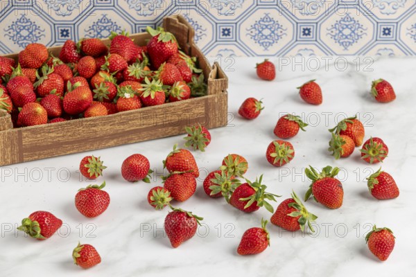 Strawberries scattered on a marble slab, next to a box full of strawberries