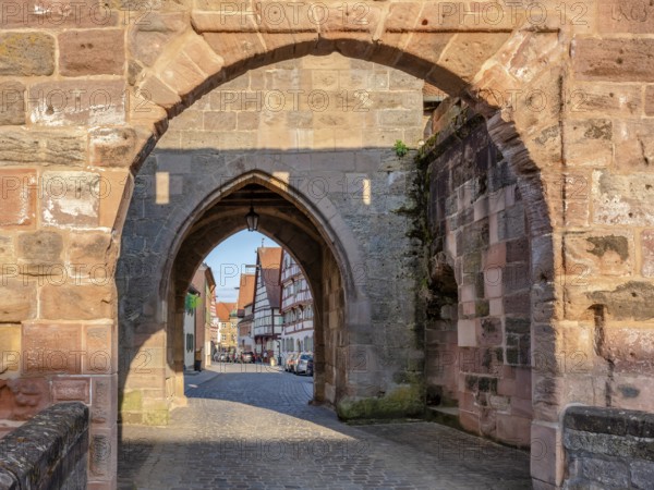 Alley with cobblestones leads through the town gate Oberes Tor, view through the gate to the half-timbered houses of the old town in the evening light, Wolframs-Eschenbach, Middle Franconia, Bavaria, Germany