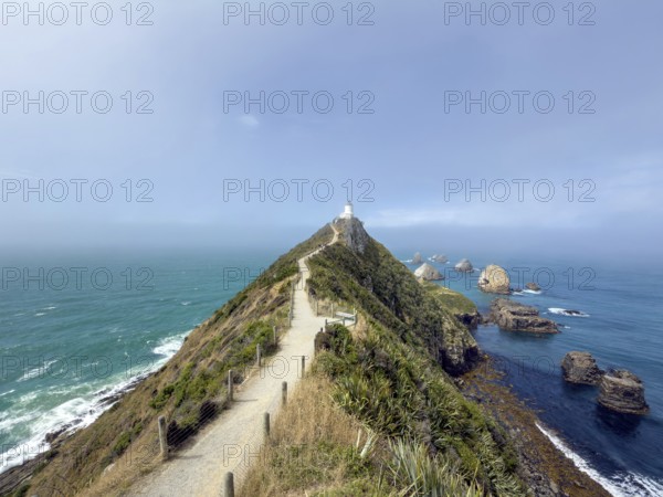 Nugget Point Lighthouse with Nugget Rocks in front of a blue sky, South Island, New Zealand, Oceania