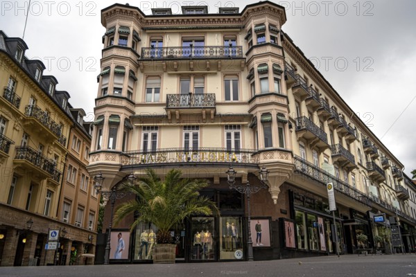 Historic building with palm trees and shop windows in an urban environment under a cloudy sky, Baden Baden, Germany