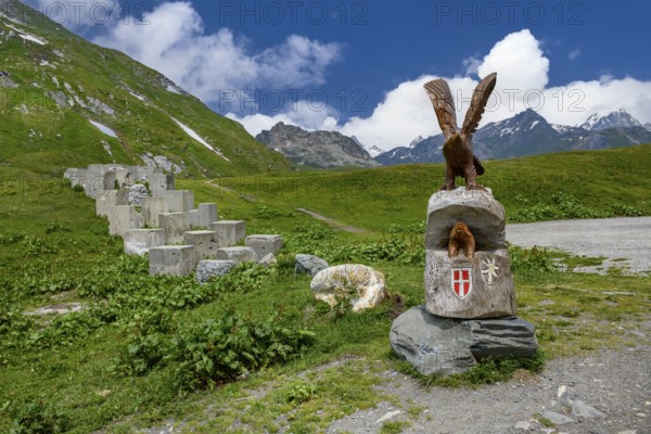 Historical border fortification from the Second World War WW II 2 on the border between France at the front and Italy at the back on the Alpine pass Kleiner Sankt St. Bernhard Colle del Piccolo San Bernardo Col du Petit Saint Bernard, on the right on the pedestal sculptures of eagle and marmot and coat of arms of the Duchy of Savoy, Graian Alps, Département Savoie, France, Aosta Valley, Italy