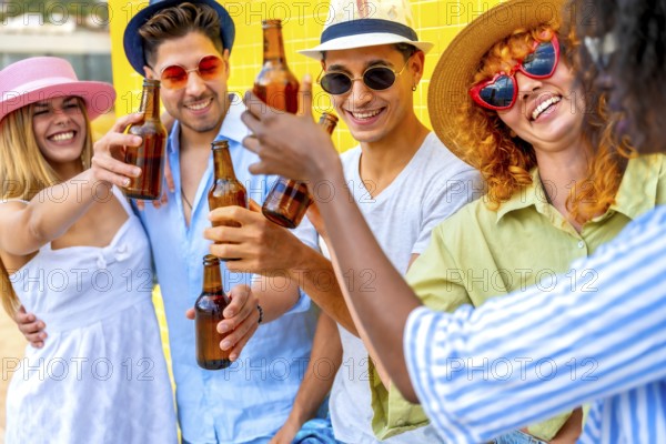 Group of cheerful multiracial young people wearing summer clothes and hats toasting and drinking beer bottles at a summer party