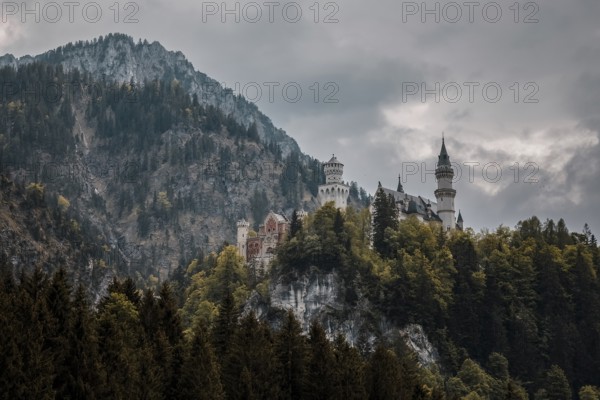 The impressive Neuschwanstein Castle on a dense, wooded hill under a dramatically cloudy sky, Schwangau, Bavaria