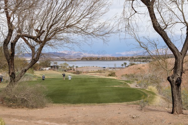 Threesome of senior golfers teeing off while playing on a golf course along the shoreline of Las Vegas Wash at Lake Las Vegas in Henderson, Nevada, USA