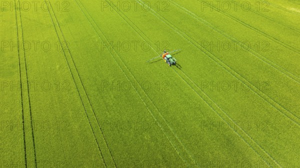 Farmer with tractor working in the field. In early summer, he fertilises the grain for an optimum yield. Drone photo. Merklingen, Baden-Württemberg, Germany