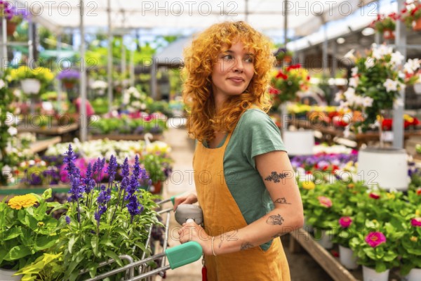 Young woman pushing a shopping cart while selecting vibrant flowers in a garden center greenhouse, enjoying a colorful spring day