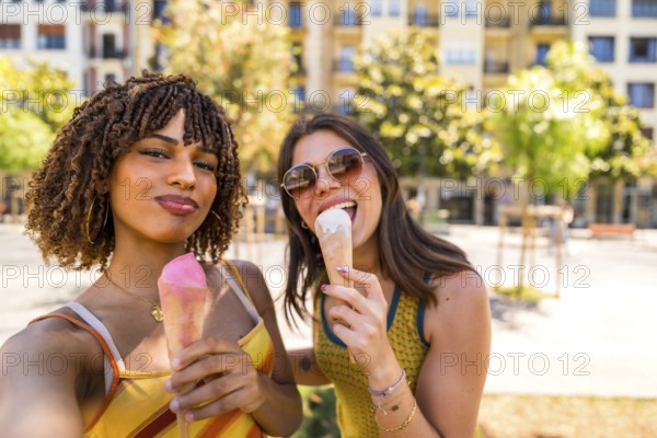 Two cheerful women enjoying ice cream cones outdoors, taking a selfie on a sunny summer day in an urban setting