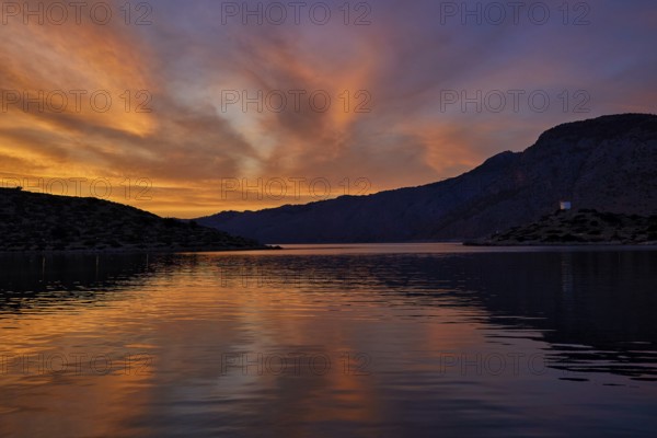 Colourful sunset over a calm lake with mountainous backdrop, Holy Week, Bay of Panormitis, Panormitis Monastery, Symi, Dodecanese, Greek Islands, Greece