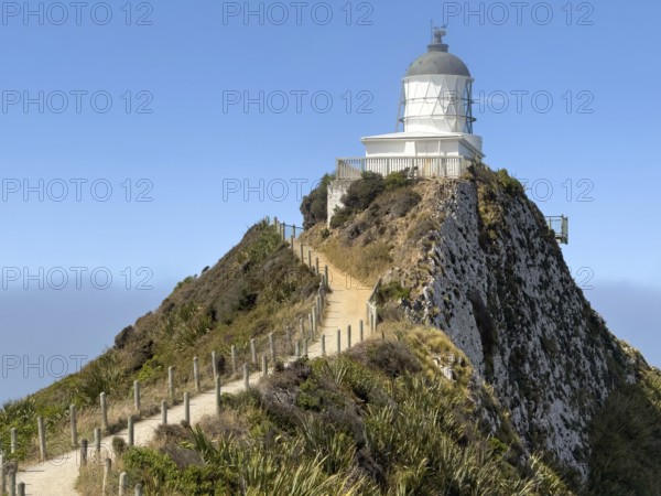 Nugget Point Lighthouse with Nugget Rocks in front of a blue sky, South Island, New Zealand, Oceania