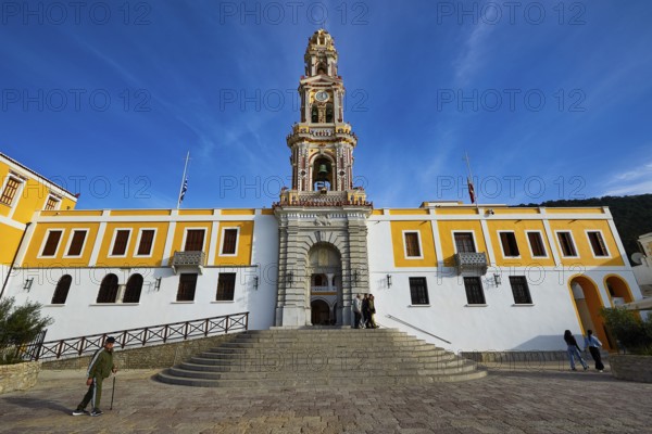 Historic building with baroque church tower and people on a square under blue sky, Holy Week, Panormitis Bay, Panormitis Monastery, Symi, Dodecanese, Greek Islands, Greece