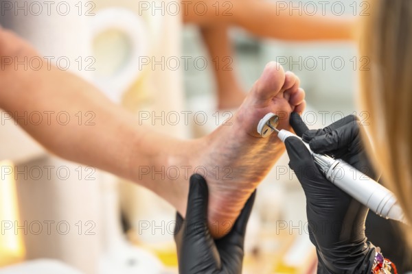 Close up of callus removal procedure being performed on foot by professional podiatrist using electric pedicure tool in beauty salon