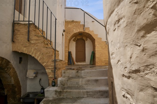 Historic courtyard with stairs, stone arches and wooden doors in the sunlight, Monastery, Moni Roukouniotis, Symi, Dodecanese, Greek Islands, Greece