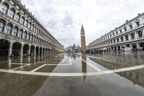 Tourists walking in flooded piazza san marco with campanile bell tower and saint mark's basilica on background in venice, italy