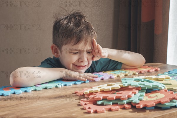 Boy with autism, expresses frustration, playing with puzzle pieces, on a wooden table, natural light, lifestyle