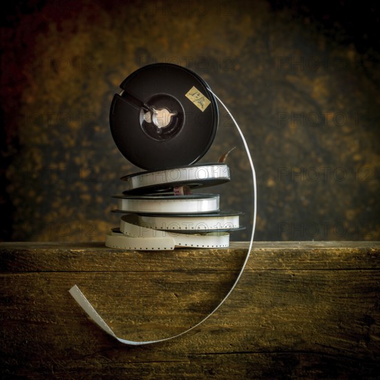 Stacked film reels rest on a worn wooden surface, highlighting the charm of vintage cinema. The reels display a classic film strip, evoking nostalgia and storytelling