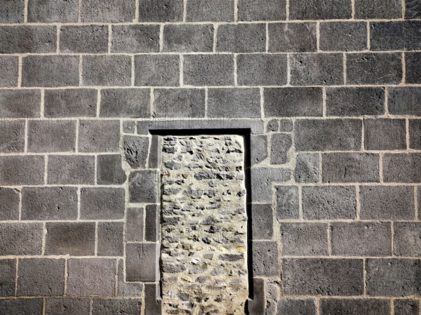 This structure features a stone wall of rough masonry with a distinct doorway outlined in rectangular shape, highlighting the contrast of textures and materials in a rustic environment