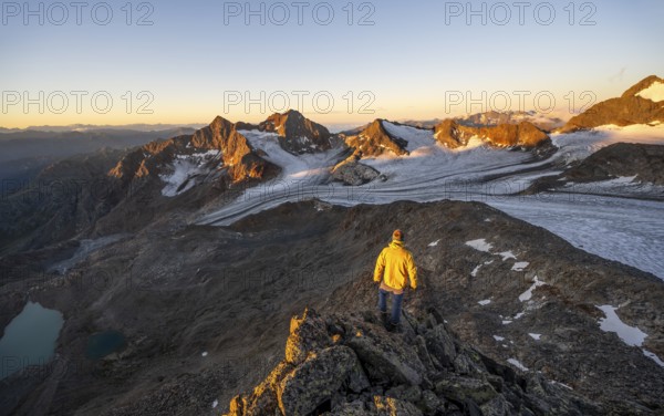 Mountaineers in front of a picturesque high mountain landscape at sunrise with alpenglow, blue glacial lakes, glaciers and rocky mountain peaks in the morning light, view at the Becher on mountain peaks Königshofspitz and Sonklarspitze and Schwarzwandspitz with glacier Übeltalferner, Stubai Alps, South Tyrol, Italy