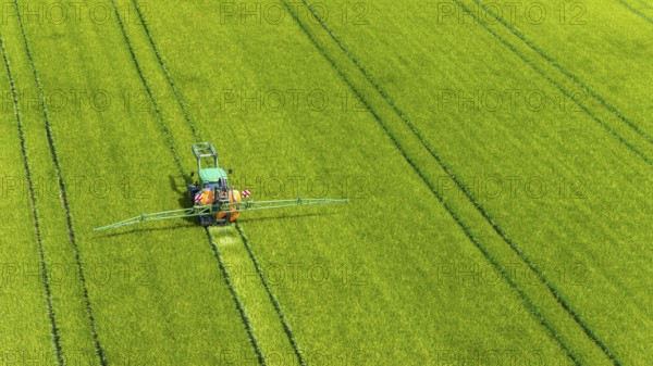 Farmer with tractor working in the field. In early summer, he fertilises the grain for an optimum yield. Drone photo. Merklingen, Baden-Württemberg, Germany