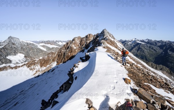 Mountaineer on rocky ridge with snow, mountain peak Wilder Freiger in the background, picturesque high mountain landscape, Stubai Alps, South Tyrol, Italy