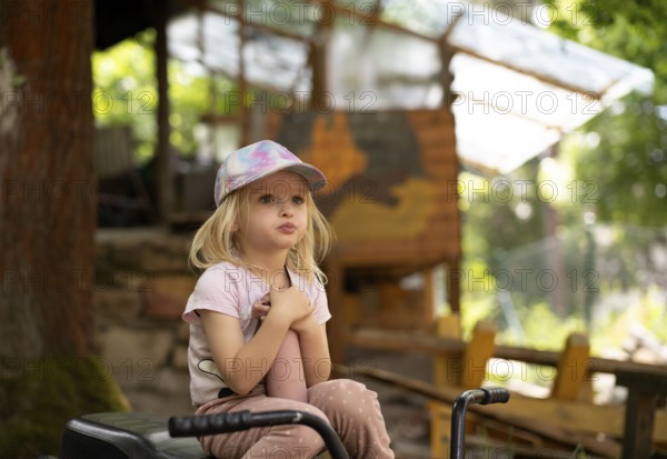 Girl, 3 years, blonde, sitting on bicycle in the garden, pensive, summer, Stuttgart, Baden-Württemberg, Germany
