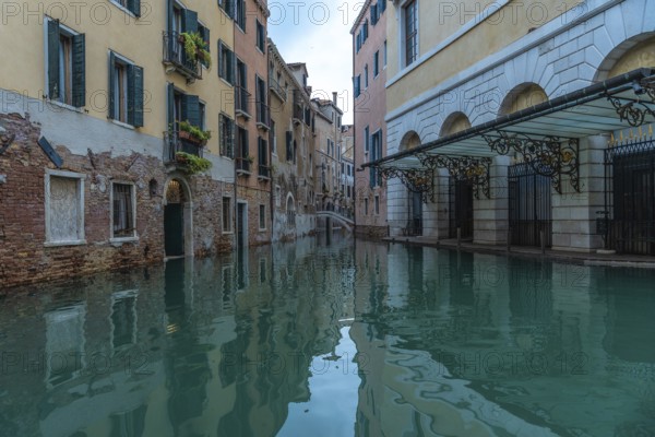 Calm water reflecting colorful buildings along a canal in venice, italy, during acqua alta, or high tide