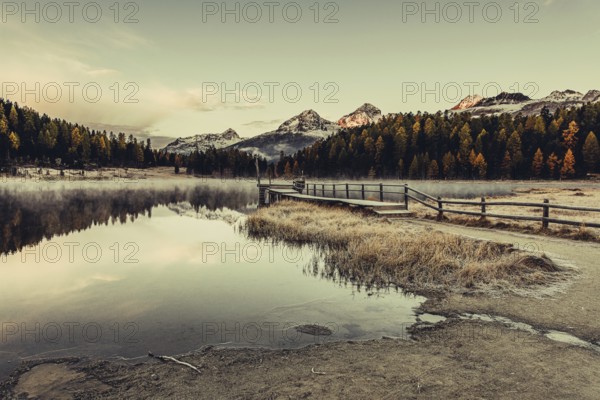 Lake Staz near Sankt Moritz in the Engadin in Switzerland. Morning atmosphere with fog in autumn. Water reflection and snow-covered mountains in the background