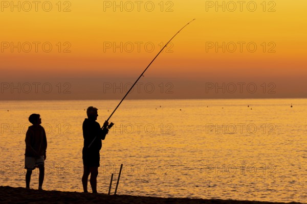 A man fishing just in front of sunrise on the Costa Rei, a coastline of the Italian island of Sardinia, in the Mediterranean Sea, Monte Nai, Costa Rei, Sardinia, Italy