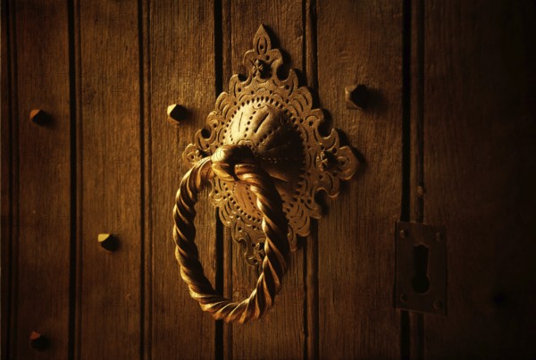 A beautifully designed door knocker sits prominently on a weathered wooden door. The warm lighting highlights the intricate patterns, revealing the craft of metalwork in a striking manner