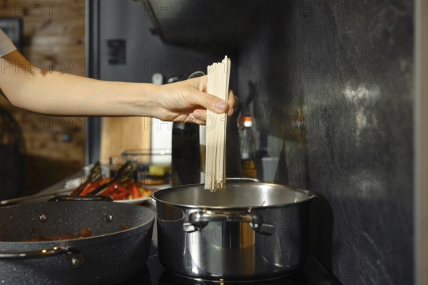 A person prepares a healthy pasta dish by adding uncooked noodles to boiling water in a contemporary kitchen