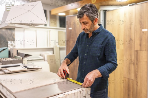 Architect choosing tile for his project, measuring large format tiles with tape measure in a home improvement store